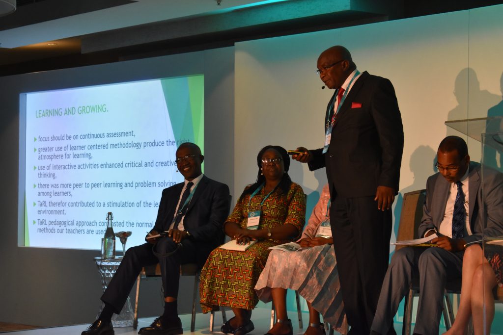 Mahuba Hazemba speaks on stage, while fellow panelists Raoul Kone, Cynthia Efua Bosumtwi-Sam, Angela Tsheole, and Habbat Abdi listen at the Teaching at the Right Level Conference in 2018.