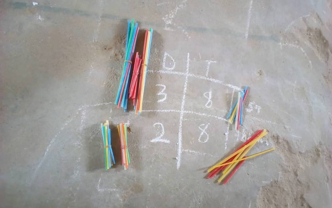 A Maths sum written on the floor in chalk, with colourful sticks beside it.