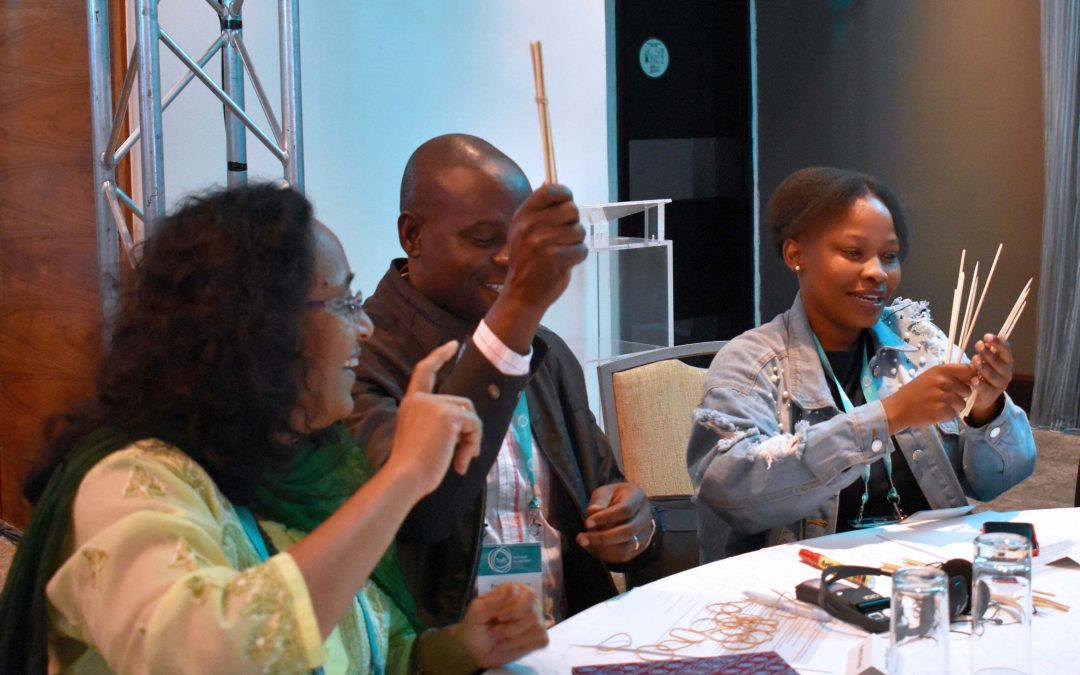 Meera Tendolkar, Fred Abungu, and Moitshepi Matsheng practice a bundle and sticks maths activity at the 2018 TaRL Conference.