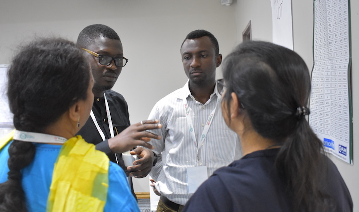 Four people stand in front of a syllable chart, having a discussion.