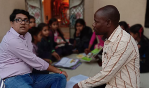 Two TaRL Africa team members sit on the floor with children who are reading.