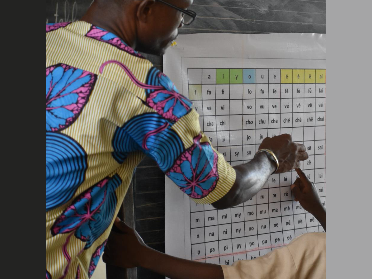 A child writes the word cesu on a mind map on a board. In the centre of the mind map is the word "cikolo".